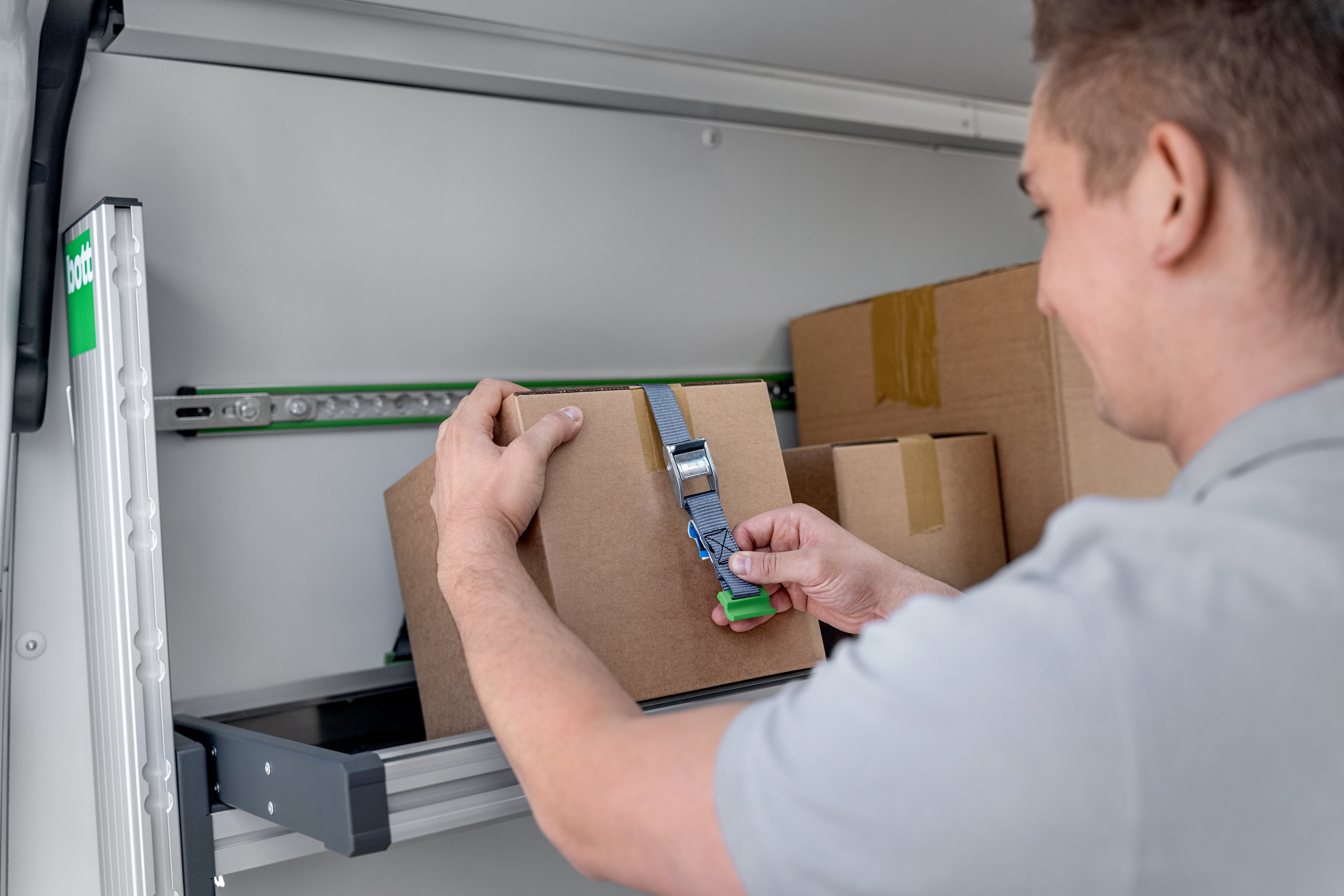 KEP-Zusteller sichert ein Paket mit einem Zurrgurt auf einem bott vario3 Klappregal.