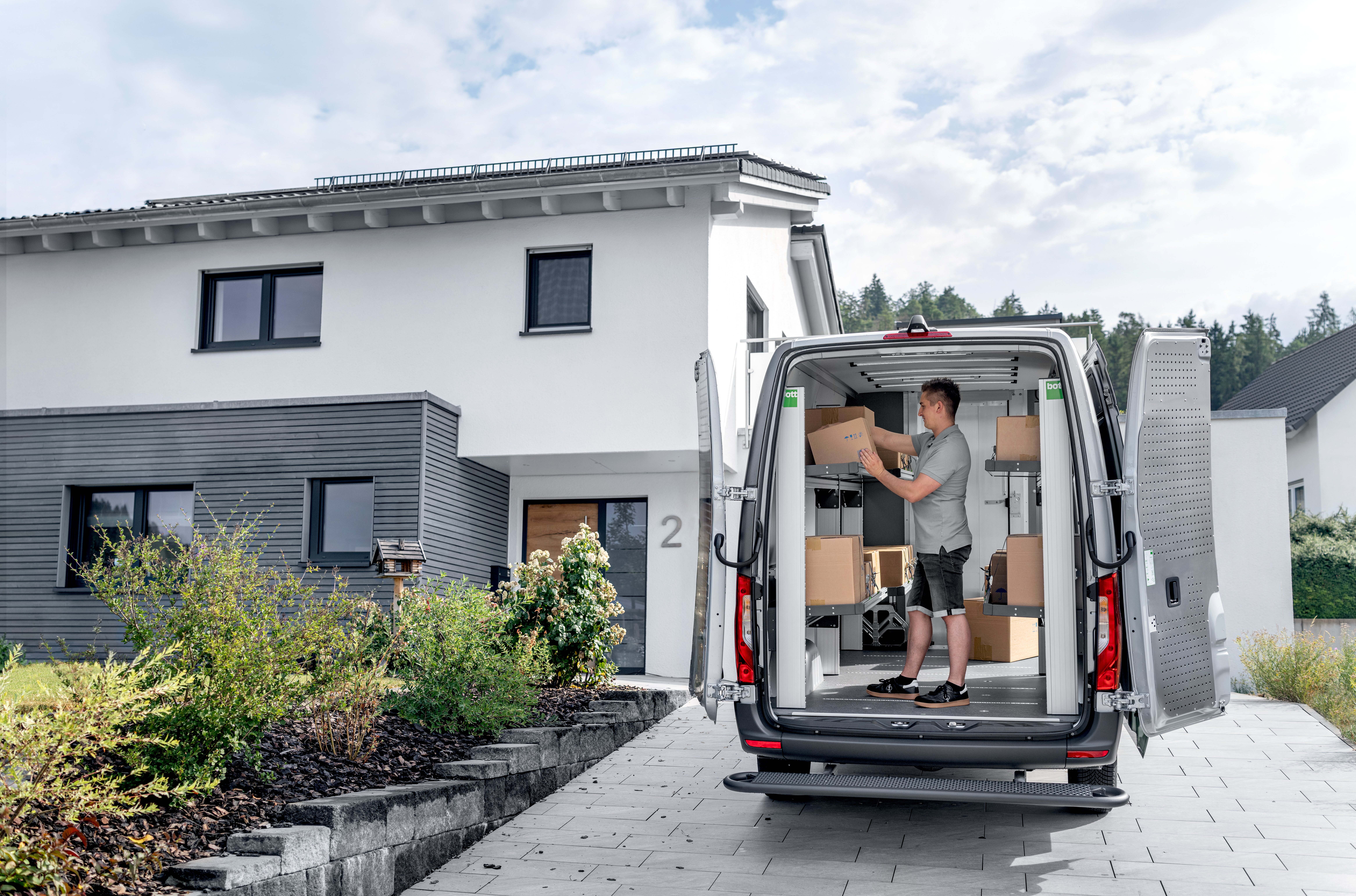 KEP-Zusteller nimmt ein Paket zwischen beladenen bott vario3 Klappregalen aus dem Transporter.